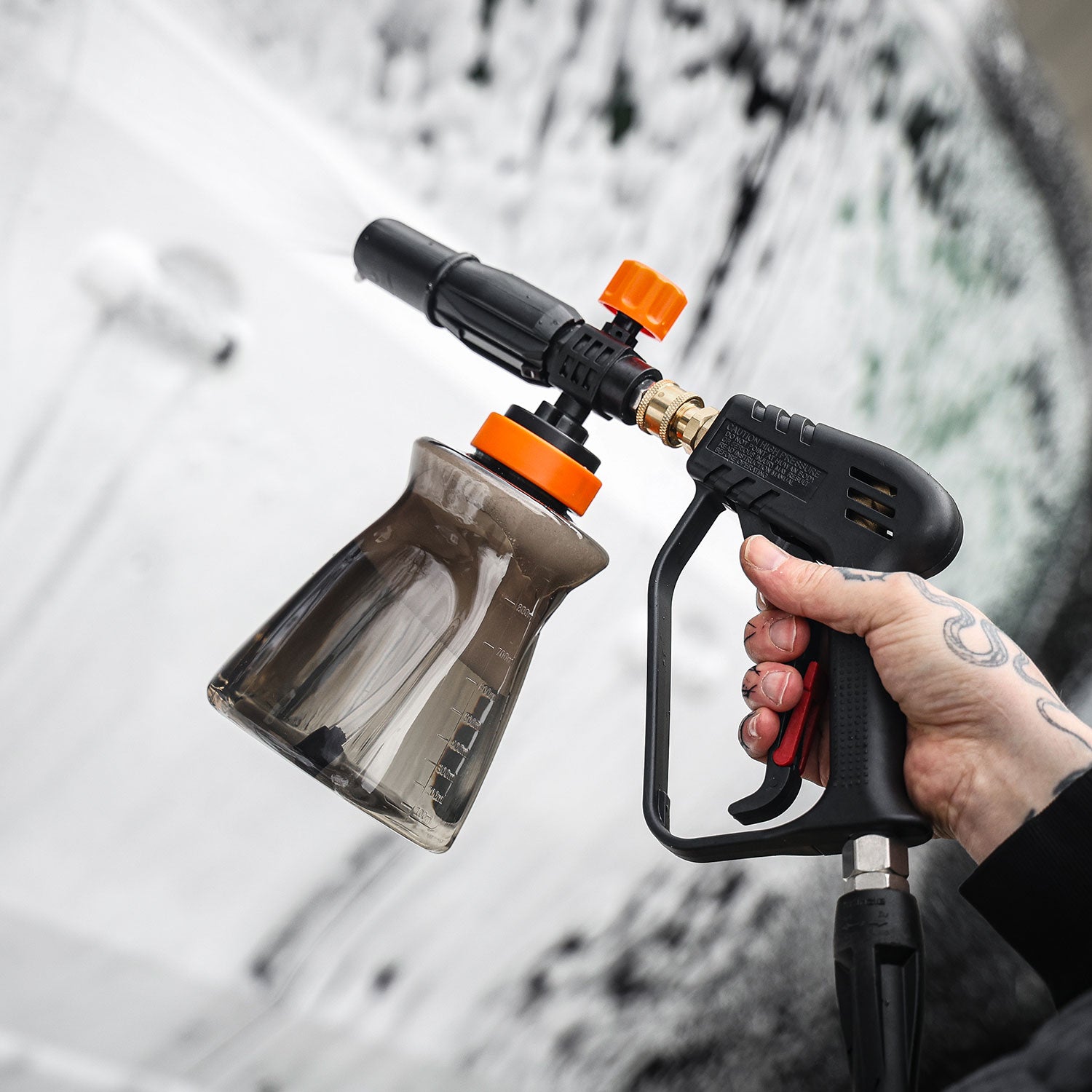 Person holding a snow foam lance and water gun against a snowy background