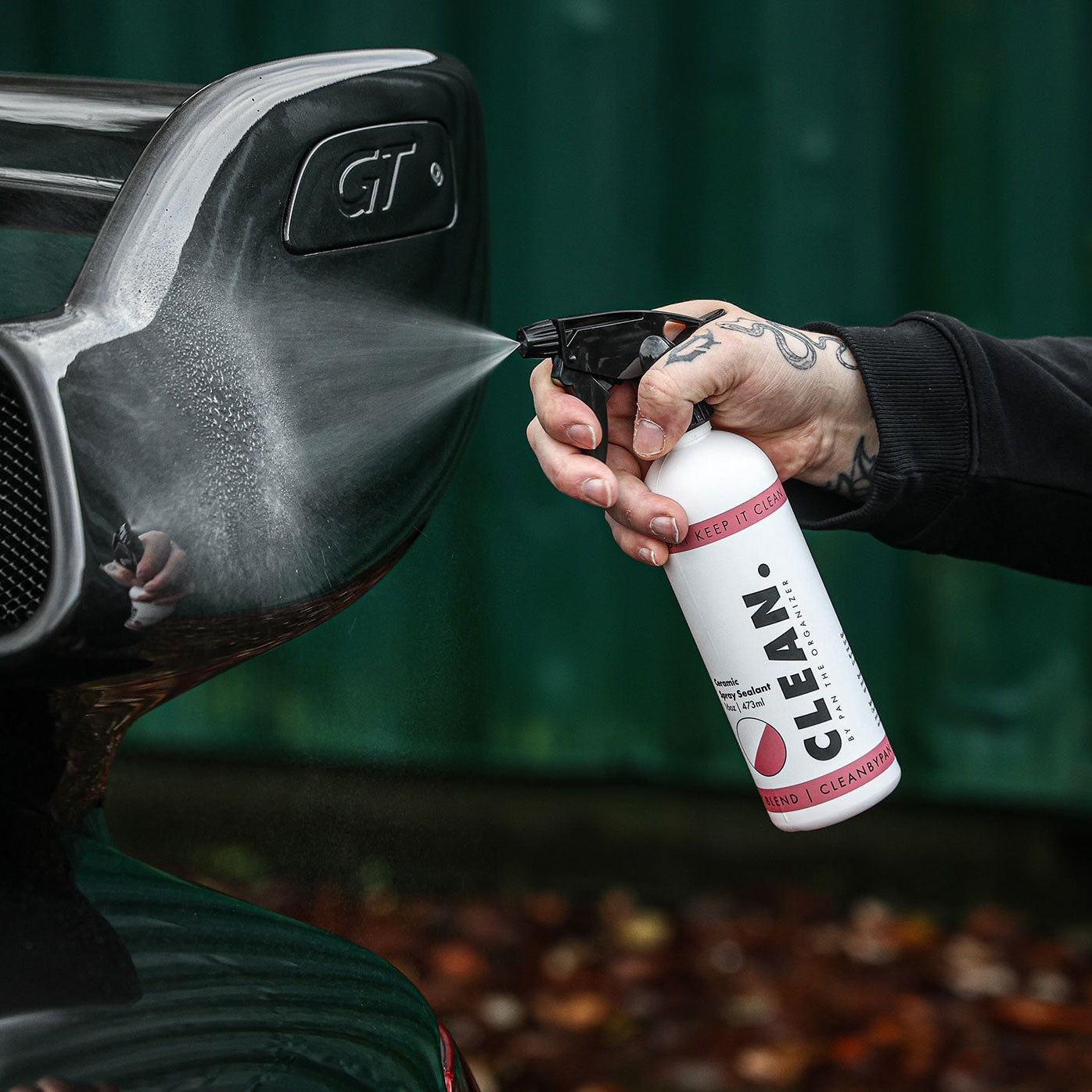Person cleaning a duck call with a spray bottle labeled 'CLEAN. By Pan  Ceramic Spray Sealant' against a blurred background