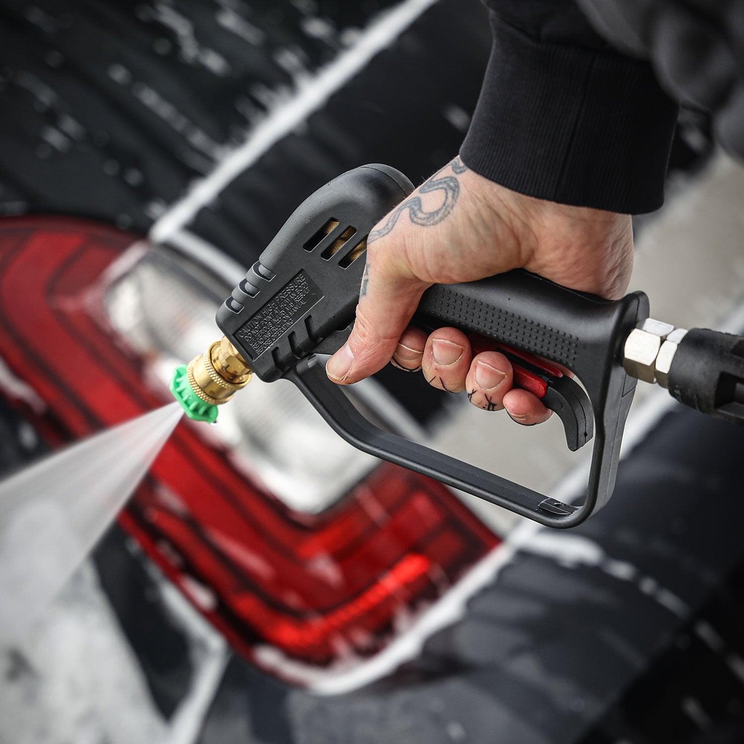 Person using a high-pressure washer to clean a vehicle